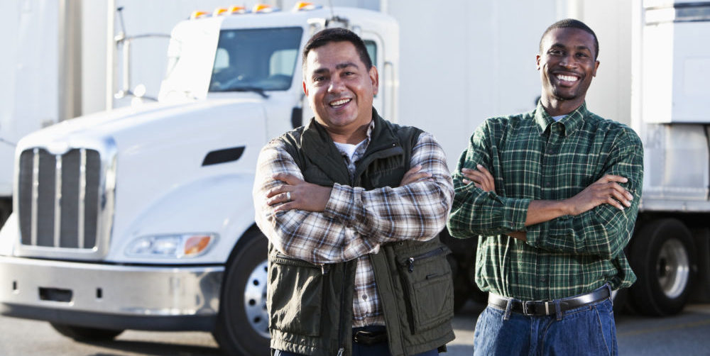 picture of Hispanic and African American truck drivers standing in front of semi-trucks.