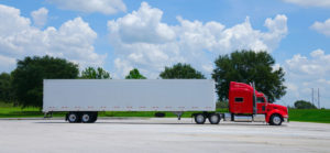 photo of a red semi tractor truck with a clean white cargo container trailer against a simple colorful background of trees and blue sky