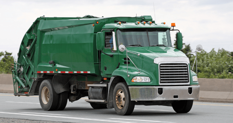 Green trash truck driving down highway