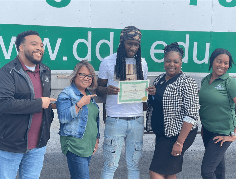 DDA graduate holding CDL certificate, instructors standing around smiling