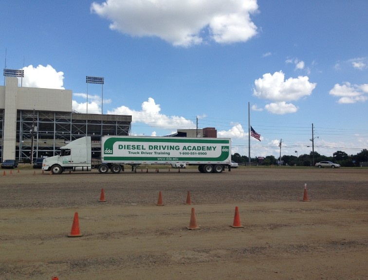 A Diesel Driving Academy semi-truck navigates a cone course at a CDL training yard
