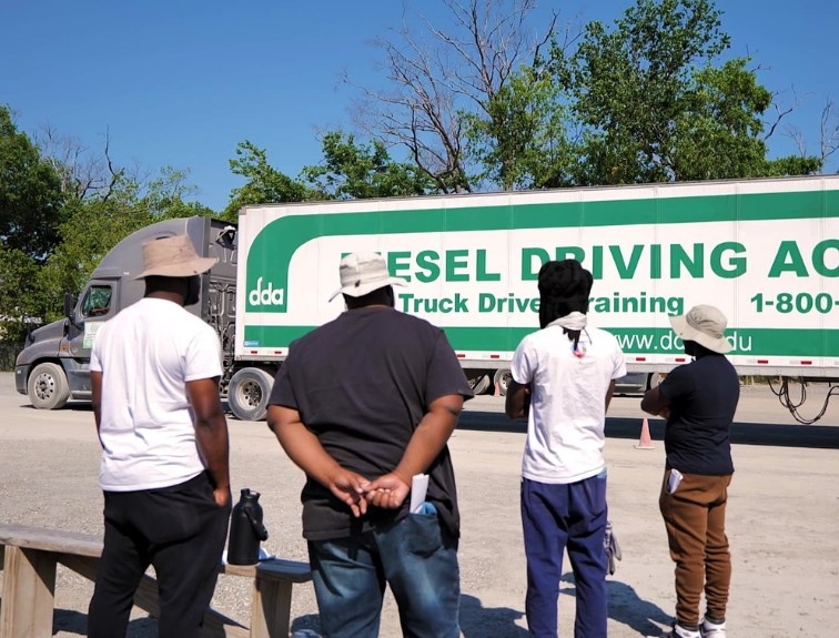 4 students standing in CDL training yard watching a truck maneuver 